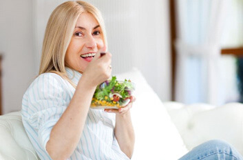 mature woman sitting on sofa, enjoying a salad