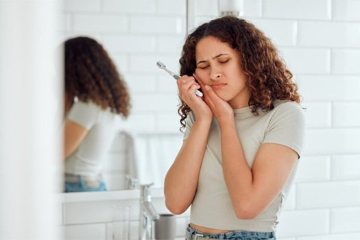 Woman rubbing her jaw while holding a toothbrush