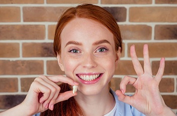 Smiling young woman holding her extracted tooth